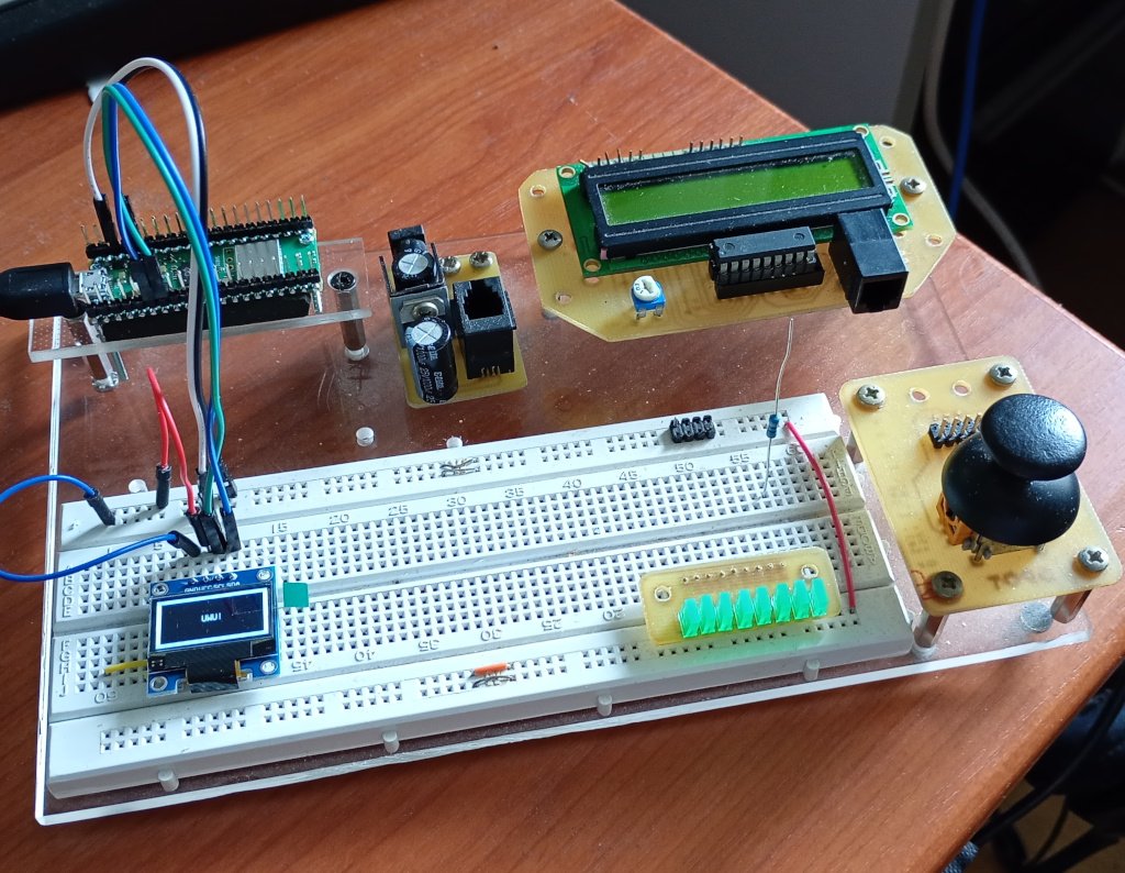 One of my breadboarding setups sitting on my desk. A variety of electronic modules are screwed onto a clear sheet of acrylic. The one item not described in the text is a module featuring a row of 8 rectangular green LEDs that plugs into the breadboard and is used for testing and monitoring.