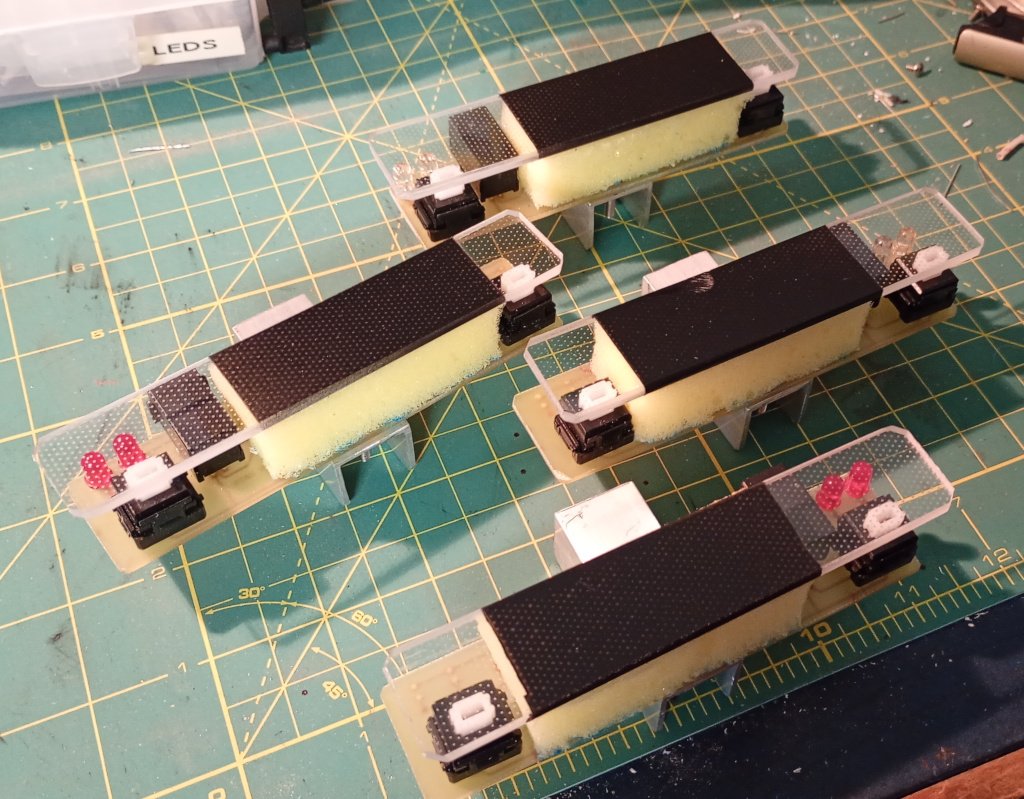 A mostly finished robot sits on a craft mat. It does not have wheels, but the sets of bumpers have been fitted to the front and rear. On the top deck a sonar turret made from circuit board material is mounted to a servo motor. The bumper modules are electrically connected to the control board with modular connectors.