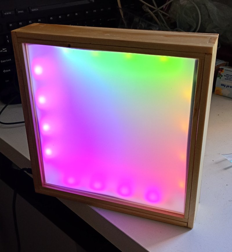 The picture shows a square wooden box sitting on a table. It is about 20 cm on each side and maybe 5 cm deep. The front face of the box is made of polycarbonate with a frosted layer behind it so that the RGB LEDs inside shine through. It is illuminated with a rainbow of magenta, cyan, green and yellow, Hope this helps.