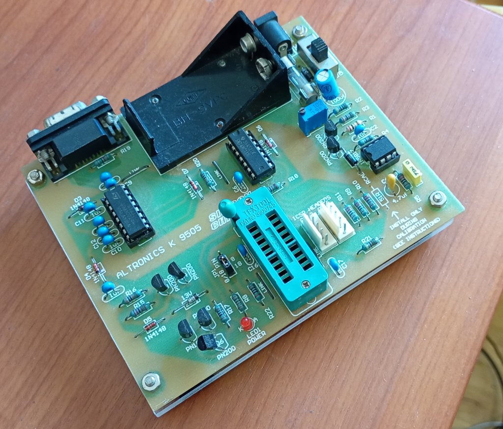 A closeup picture of an Altronics K9505 PIC programmer board. It's a circuit board with a bunch of components on it, but of interest it has a DB9 serial connector linked to a MAX232, a ZIF socket for the PIC chips being programmed and a 9v battery housing as well as resistors and transistors and so on.