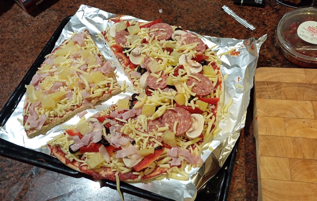 It is a pizza on an oven tray ready for baking. A third has been cut out and has ham and pineapple, The rest has a bunch of other ingredients like pepperoni, olives and mushrooms.