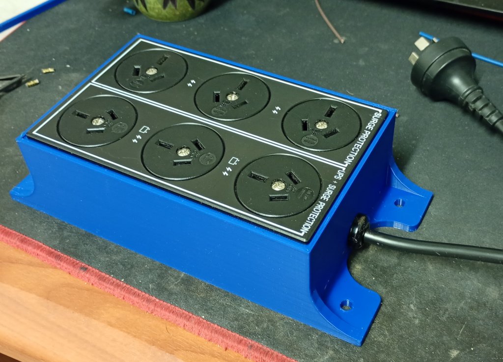 The finished power board is sitting on my desk mat. The panel of 6 mains plugs has been clipped into place in the enclosure and the black mains cord has been secured with a strain relief clamp in the provided hole. It looks pretty awesome.