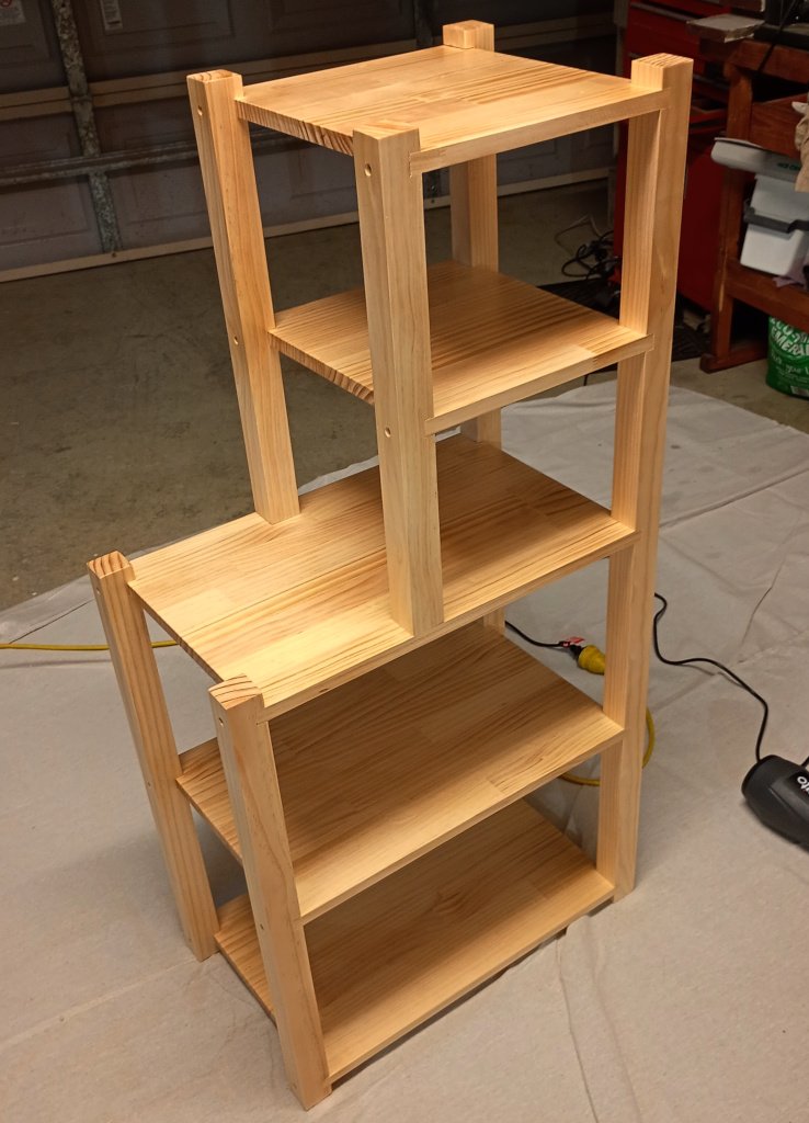 A set of shelves in the garage. It has 5 tiers of manufactured pine board joined to vertical pieces of pine. The top two shelves are half width and the bottom three shelves are full width, so the shelves look a bit like a backwards L.