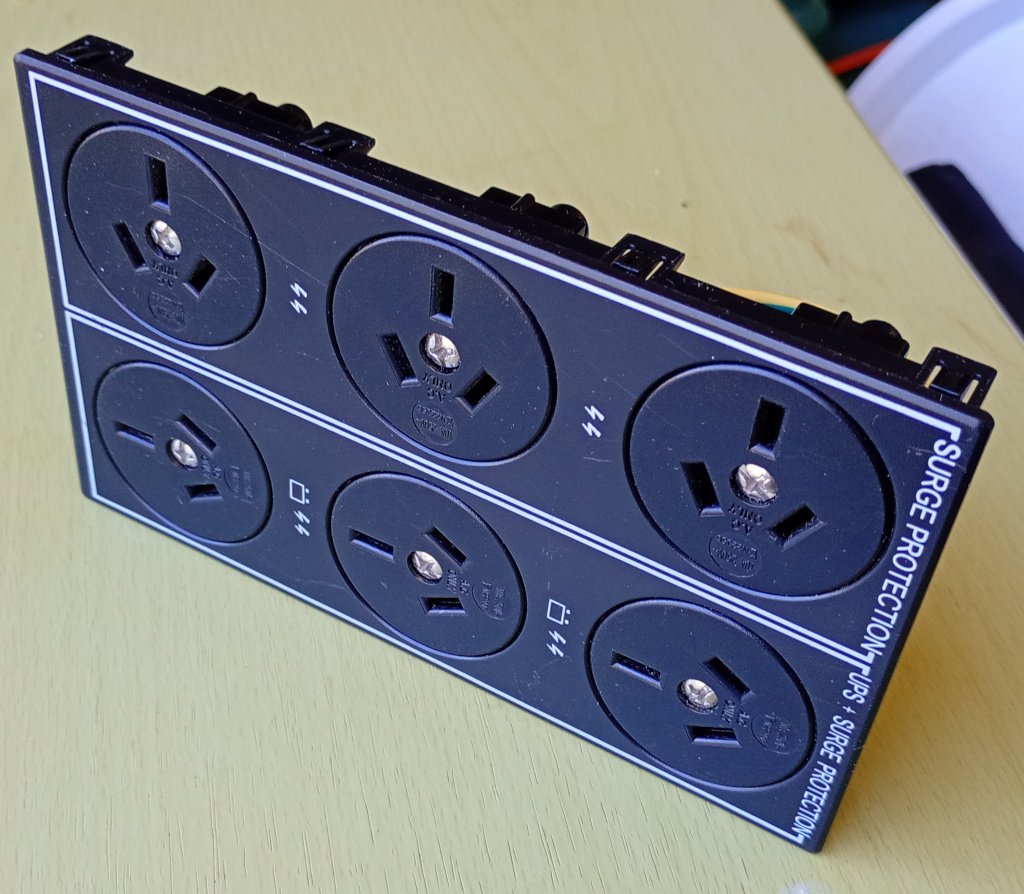 The power socket panel from a UPS, sitting on a desk. There are 6 3 pin mains sockets. This is the part I salvaged and decided to use in this project.