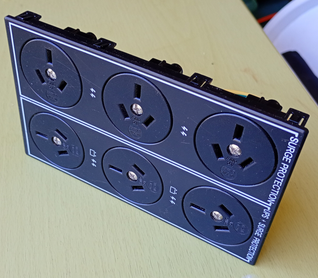 The power socket panel from a UPS, sitting on a desk. There are 6 3 pin mains sockets. This is the part I salvaged and decided to use in this project.