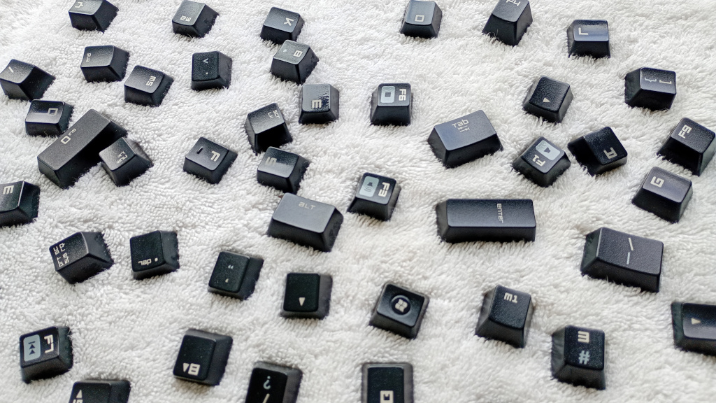 A bunch of black key caps are sitting on a white towel after being washed in the sink.