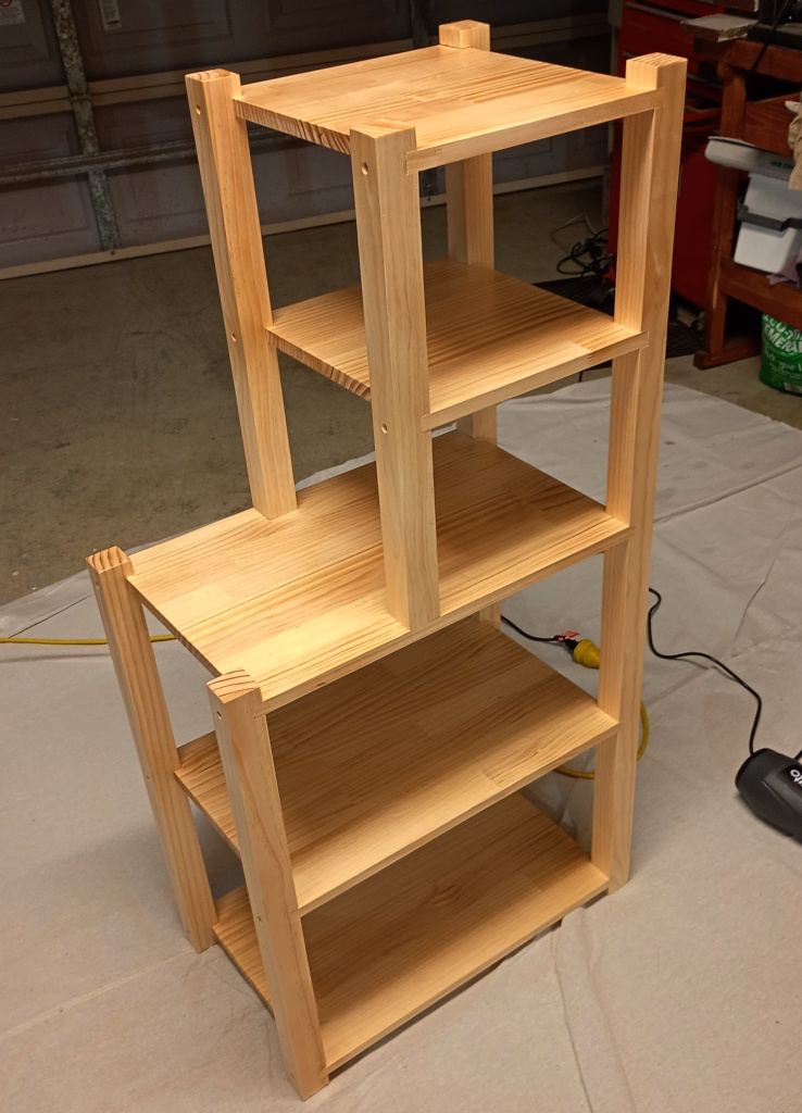 A set of shelves in the garage. It has 5 tiers of manufactured pine board joined to vertical pieces of pine. The top two shelves are half width and the bottom three shelves are full width, so the shelves look a bit like a backwards L.